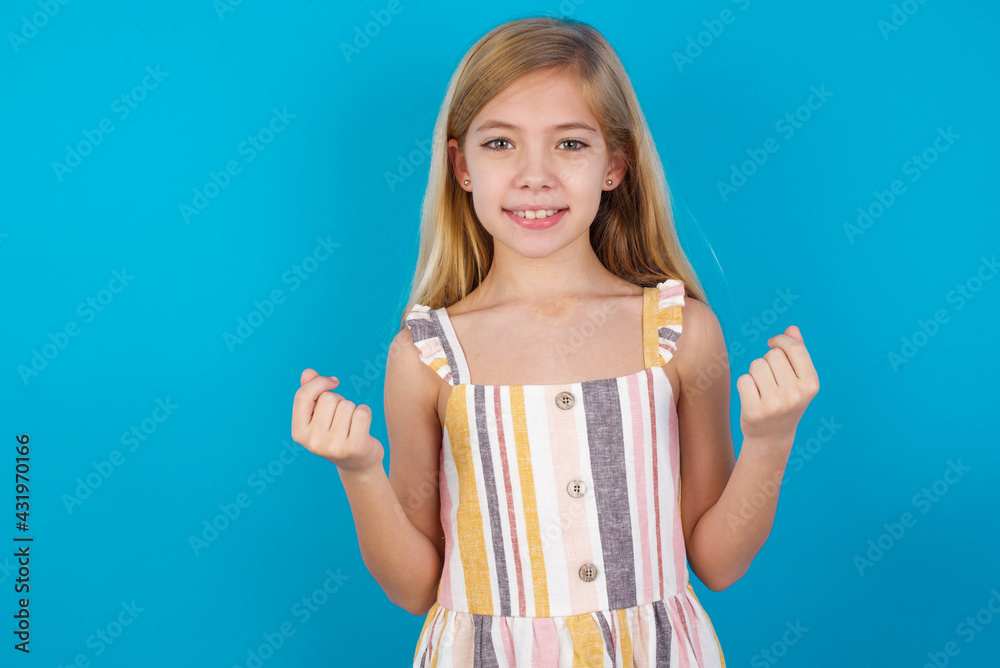 beautiful Caucasian little girl wearing stripped dress over blue background, making money gesture.