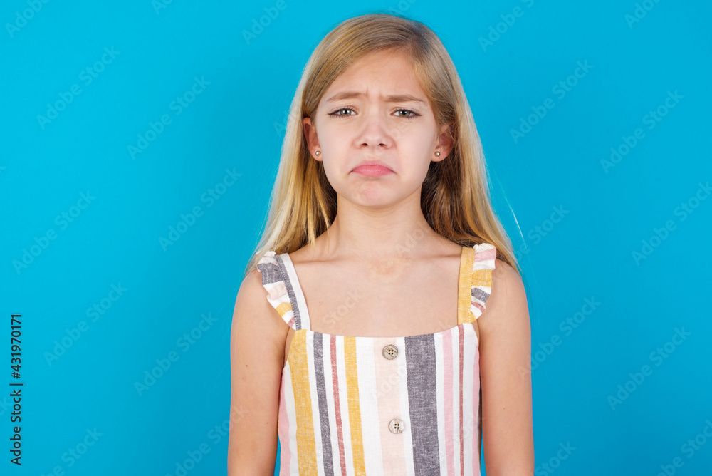 beautiful Caucasian little girl wearing stripped dress over blue wall