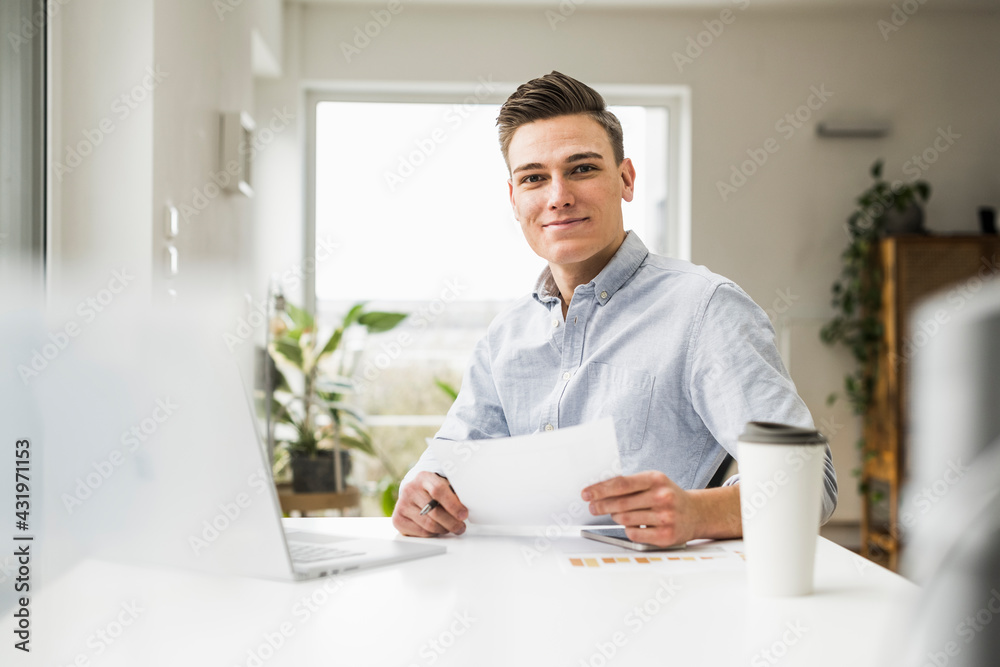 Young male entrepreneur with document sitting in home office Young male entrepreneur with document sitting in home office