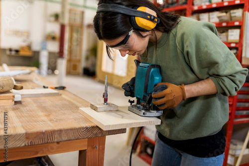 Female carpenter working with router jig at workbench in industry photo