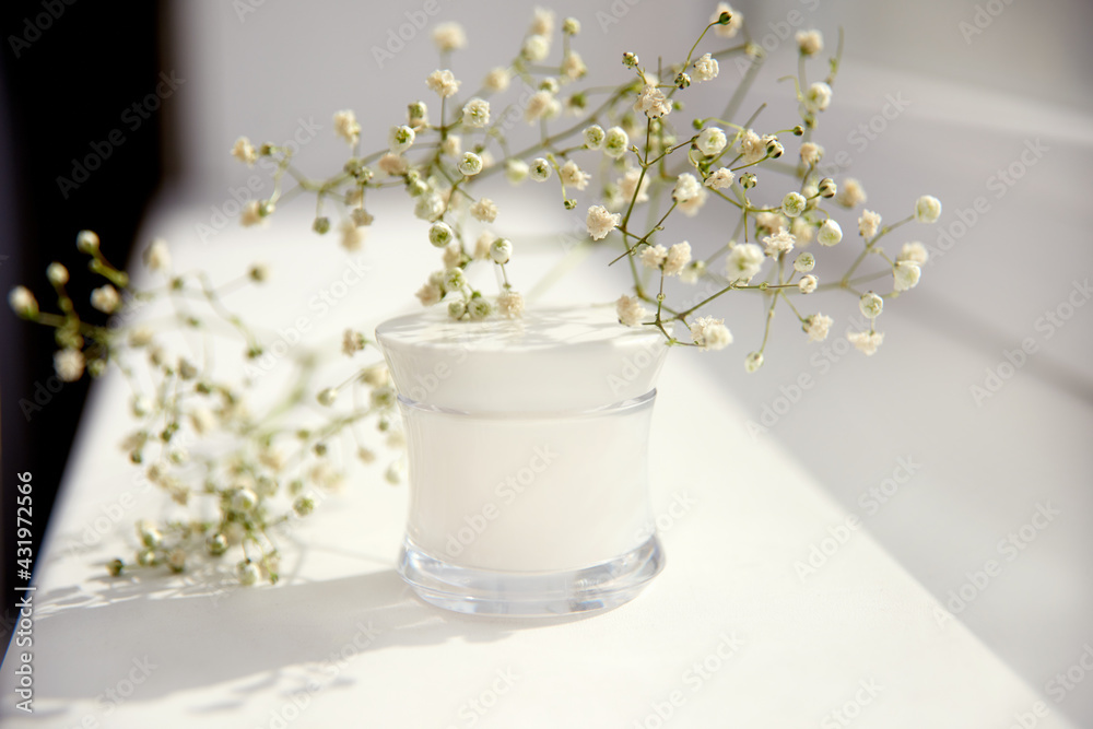 mockup moisturizer cream in glass jar and gypsophila on white background. Natural organic spa cosmetics concept.