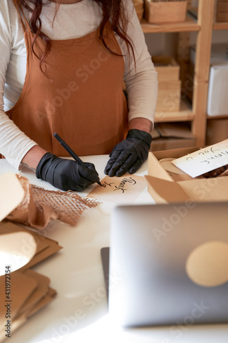 Female entrepreneur writing thank you note to put it in order packaging at workshop