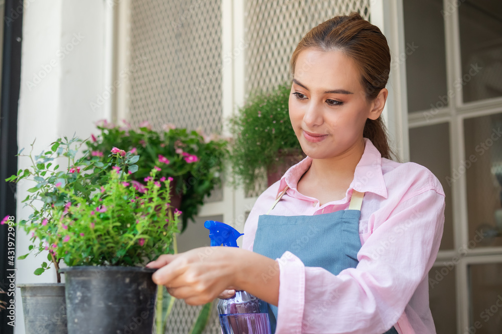 Smiling, happy young asian woman, girl gardener holding a water sprayer to water the plants with a spray in free time activities, sunshine in the morning at home, house.Lifestyle,hobby people concept. Smiling, happy young asian woman, girl gardener holding a water sprayer to water the plants with a spray in free time activities, sunshine in the morning at home, house.Lifestyle,hobby people concept.