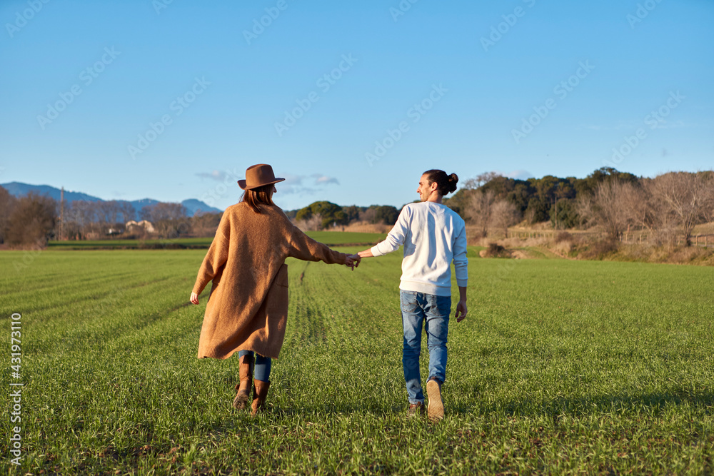 Boyfriend holding girlfriend's hand while walking on green field during sunset Boyfriend holding girlfriend's hand while walking on green field during sunset
