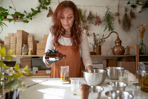 Mature woman pouring essential oil in beaker at workshop photo