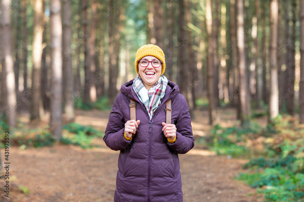 Happy woman in warm clothing holding backpack while standing in forest Happy woman in warm clothing holding backpack while standing in forest