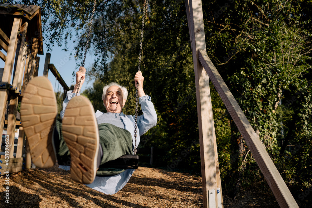 Senior man sticking out tongue while playing on swing at park Senior man sticking out tongue while playing on swing at park