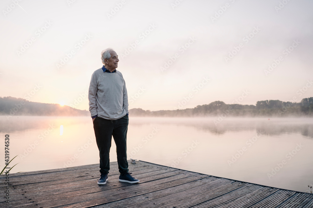 Senior man with hands in pockets looking away while standing on pier Senior man with hands in pockets looking away while standing on pier