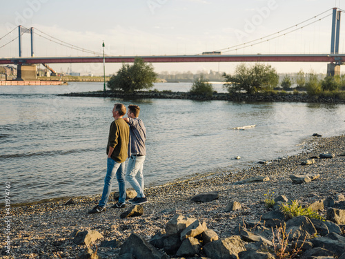 Father and son admiring river while standing against sky photo