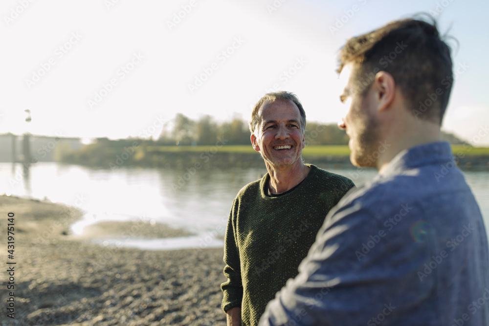 Happy father talking with son at riverbank on sunny day Happy father talking with son at riverbank on sunny day