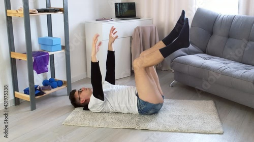 Funny nerd man in glasses is shaking his legs and hands lying on floor relaxing after fitness exercises at home. Training workout sport humor freak comic concept. Newcomer, beginner in sport.