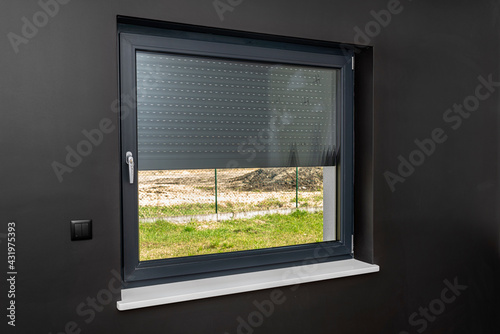 A large window in a room with black walls, half covered with external blinds. photo