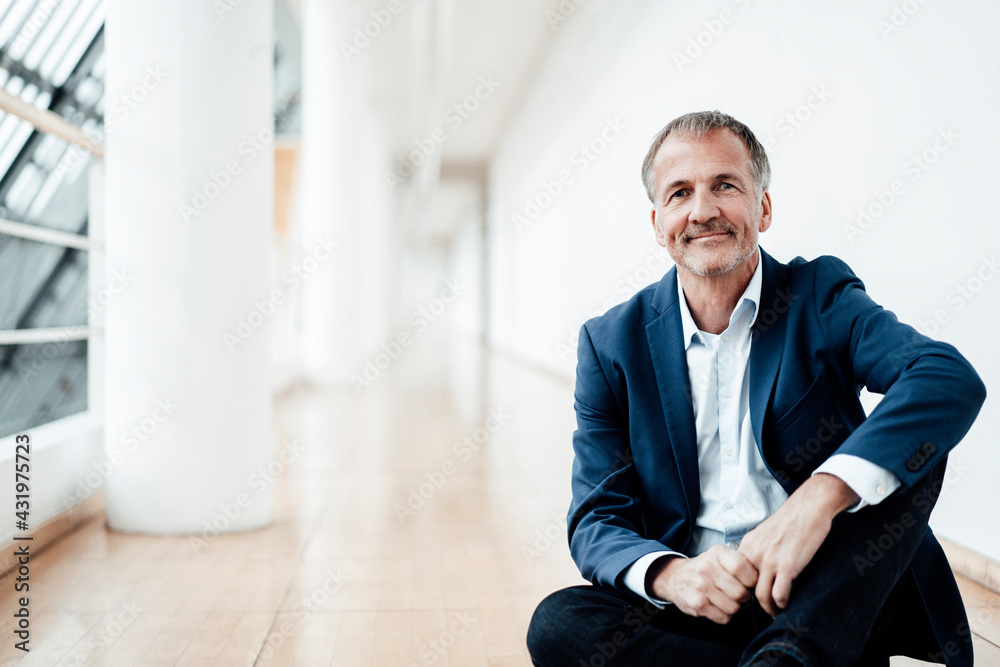 Smiling businessman sitting on floor in office cafeteria Smiling businessman sitting on floor in office cafeteria