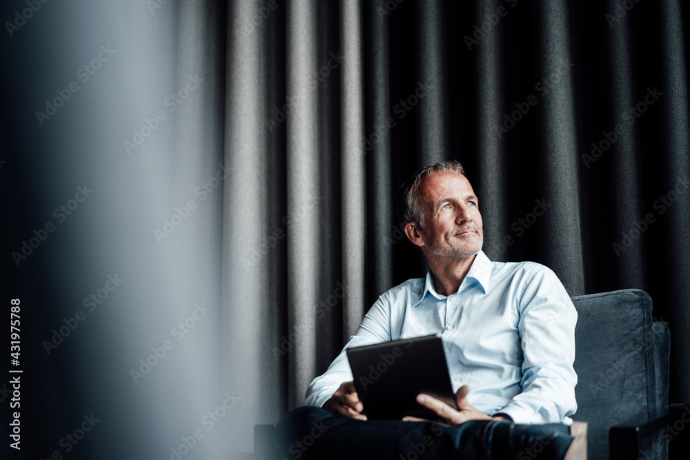 © Gustafsson/Westend61 - Contemplating businessman with digital tablet looking away while sitting on armchair in office cafeteria