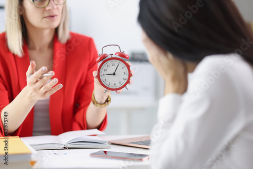 Manager shows alarm clock to subordinate, fixing delay for work photo