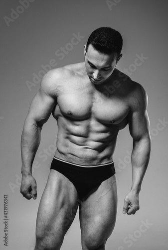 A young athlete bodybuilder poses in the studio topless, showing off his abs and muscles. Black and white.
