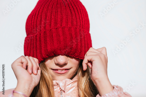 Playful girl covering eyes through knit hat against wall photo