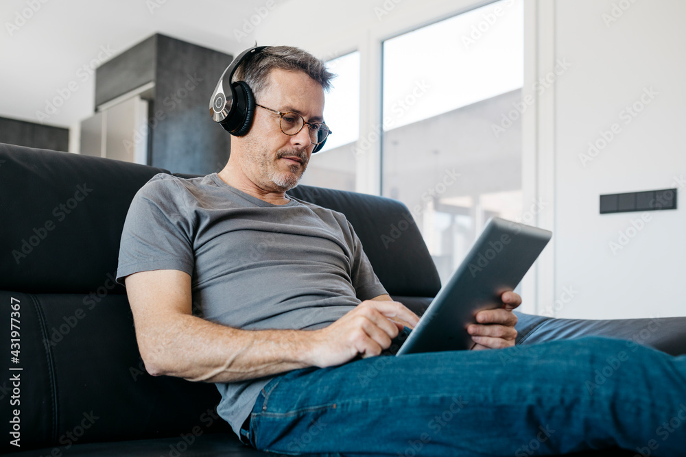 Mature man wearing headphones while using digital tablet in living room Mature man wearing headphones while using digital tablet in living room