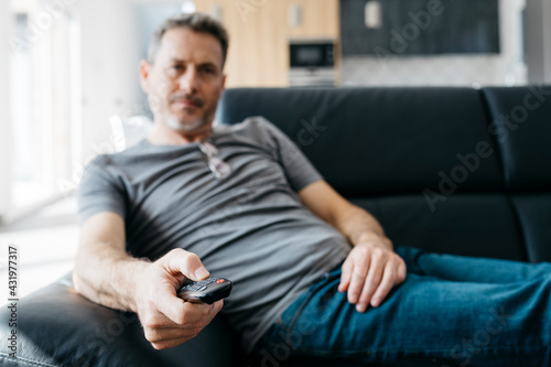 Mature man changing channels through remote control on sofa in living room photo