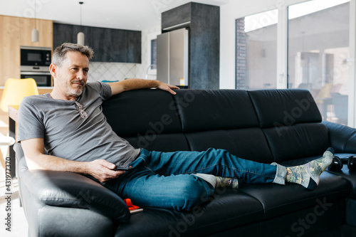 Mature man holding remote control while sitting on sofa at home photo