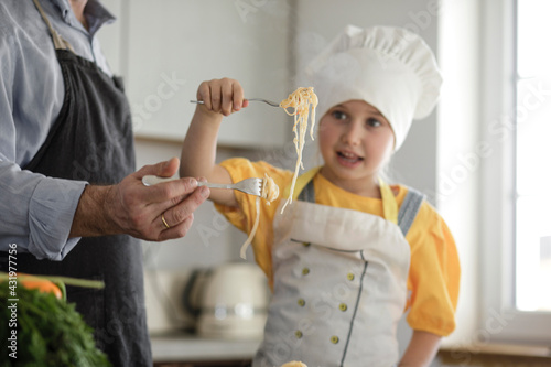 Girl wearing apron eating noodle while standing by father at home photo