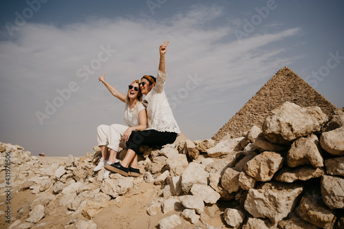 Egypt, Cairo, Two female tourists sitting together on rocks with Great Pyramid of Giza in background photo