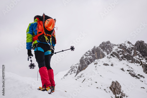 Mature man carrying backpack while walking on snowcapped mountain with crampon and hiking poles