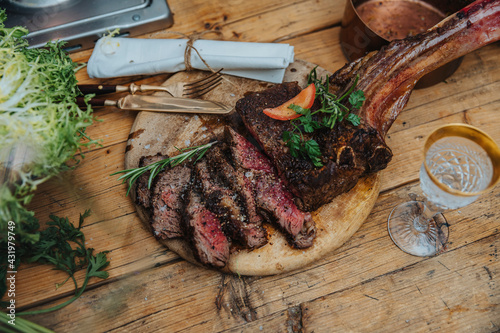 Tomahawk steak garnished with vegetables on wooden plate by drink in kitchen
