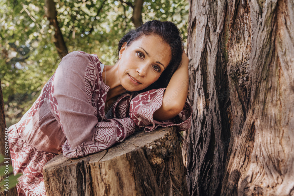 Mature woman staring while resting on tree trunk at park Mature woman staring while resting on tree trunk at park