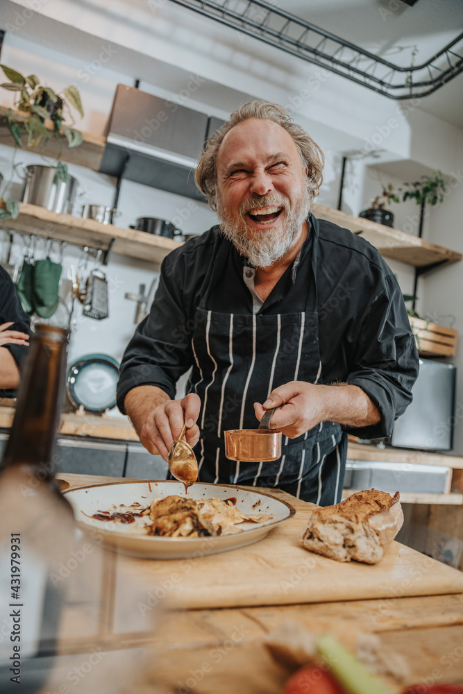 Smiling chef putting sauce over meat while standing in kitchen Smiling chef putting sauce over meat while standing in kitchen