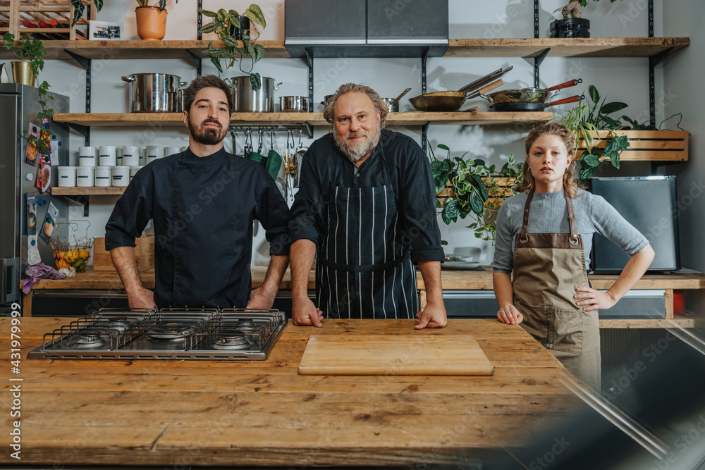 Confident chefs staring while standing by kitchen counter in kitchen