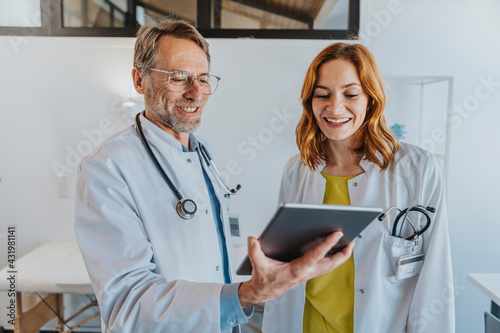 Smiling coworker using digital tablet while standing at clinic photo