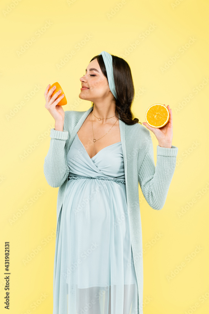 pleased pregnant woman enjoying flavor of juicy orange isolated on yellow. pleased pregnant woman enjoying flavor of juicy orange isolated on yellow.