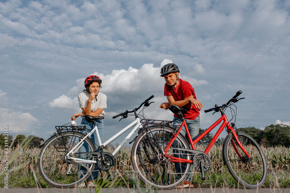 Daughter with father leaning on bicycle while standing at agricultural field against cloudy sky Daughter with father leaning on bicycle while standing at agricultural field against cloudy sky