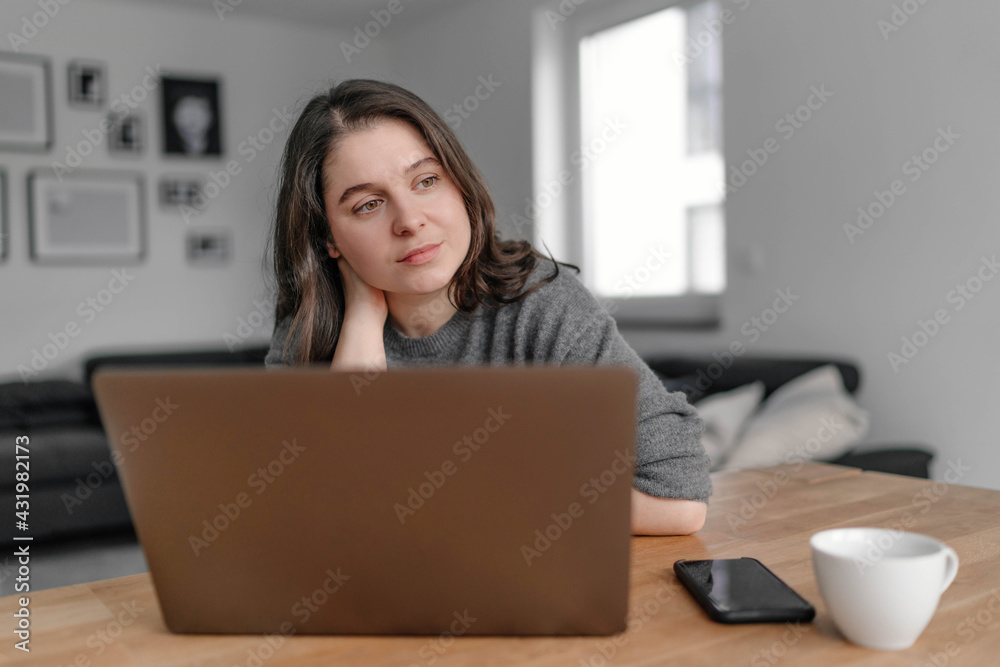 Thoughtful female professional looking away while sitting with laptop at home Thoughtful female professional looking away while sitting with laptop at home