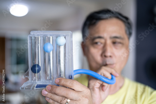 Old man uses a Tri-ball Incentive Spirometer for check his lung function.