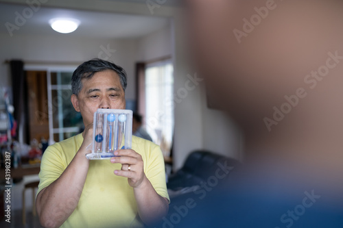 Old man uses a Tri-ball Incentive Spirometer for check his lung function. photo