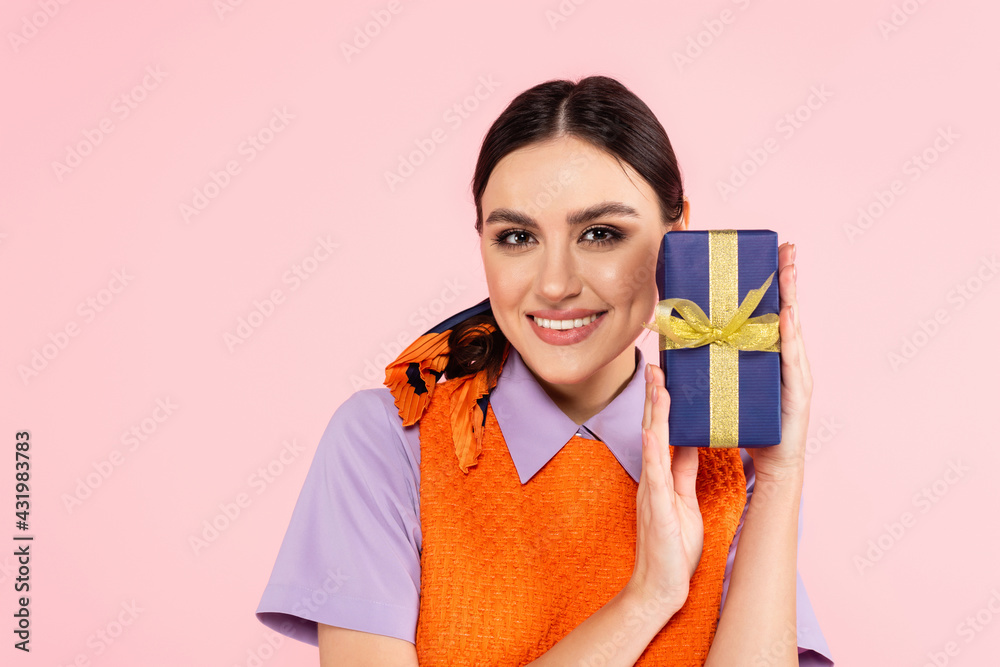 joyful woman looking at camera while showing present isolated on pink. joyful woman looking at camera while showing present isolated on pink.