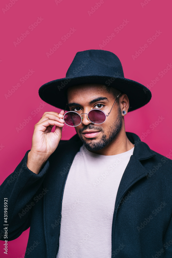 Man in hat adjusting sunglasses against pink background Man in hat adjusting sunglasses against pink background