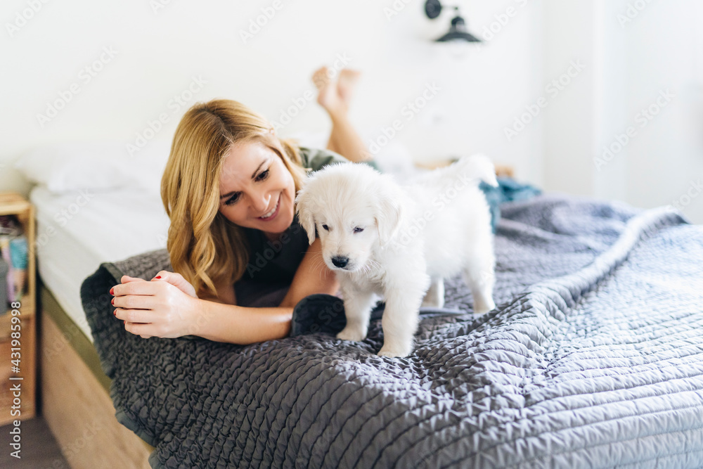 Smiling woman looking at Golden Retriever puppy while lying on bed Smiling woman looking at Golden Retriever puppy while lying on bed