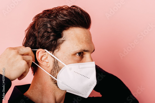 Businessman wearing white protective face mask while standing against colored background
