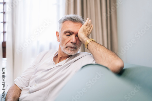 Tired man rubbing eyes while sitting on sofa in hotel room photo