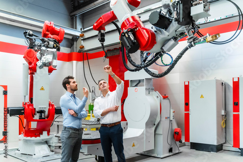 Mature entrepreneur discussing over robotic welding torch with colleague in factory