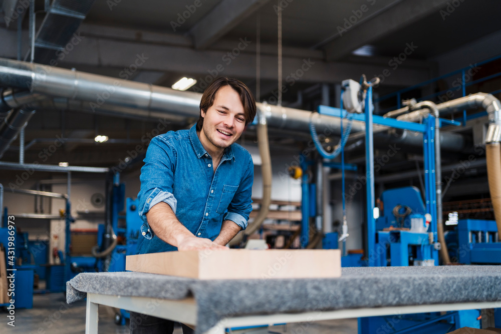 Smiling manual worker examining plank while standing at industry Smiling manual worker examining plank while standing at industry