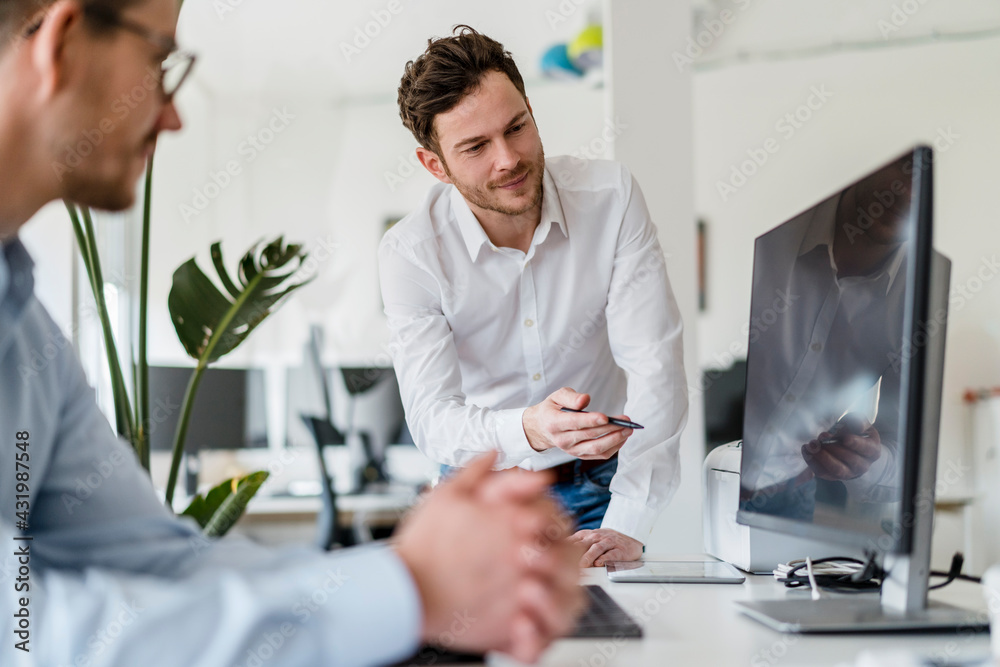 Male entrepreneur discussing over computer with colleague in office Male entrepreneur discussing over computer with colleague in office