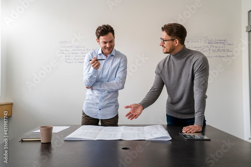 Business people discussing over blueprint during meeting at office against wall