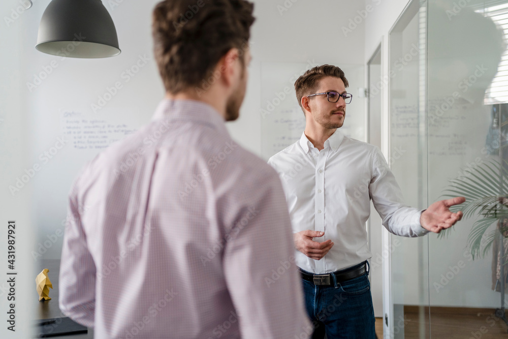 Businessman explaining male colleague in office Businessman explaining male colleague in office