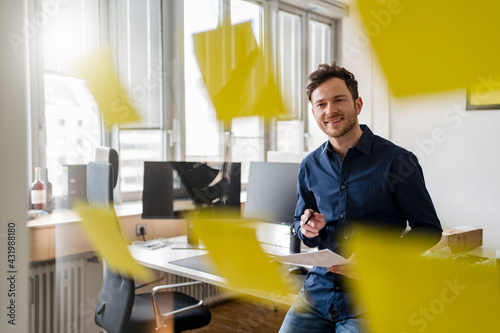 Smiling businessman with document looking at adhesive notes at office photo