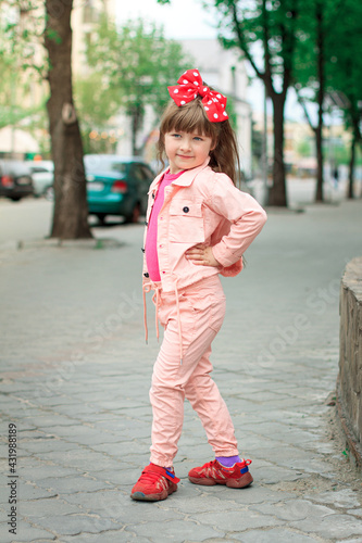 Full-length portrait of a little girl in a pink suit on a city street