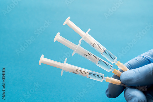 Hand of person wearing protective glove holding three syringes photo
